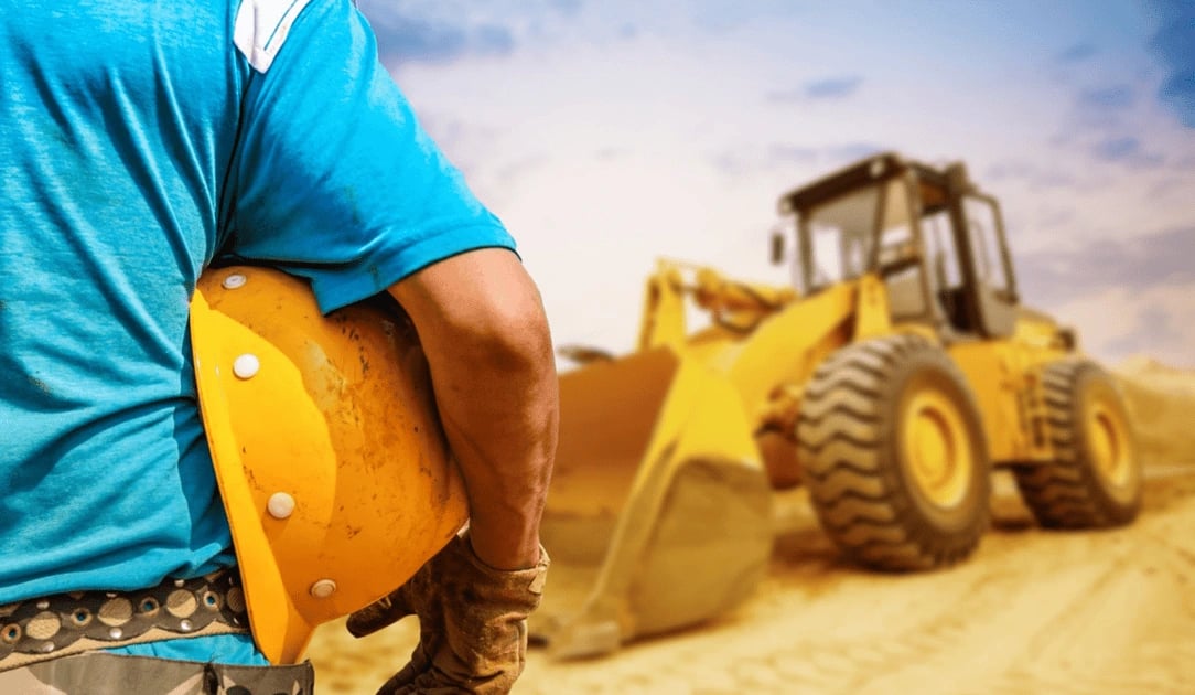 A man holding his hard hat in front of a tractor.