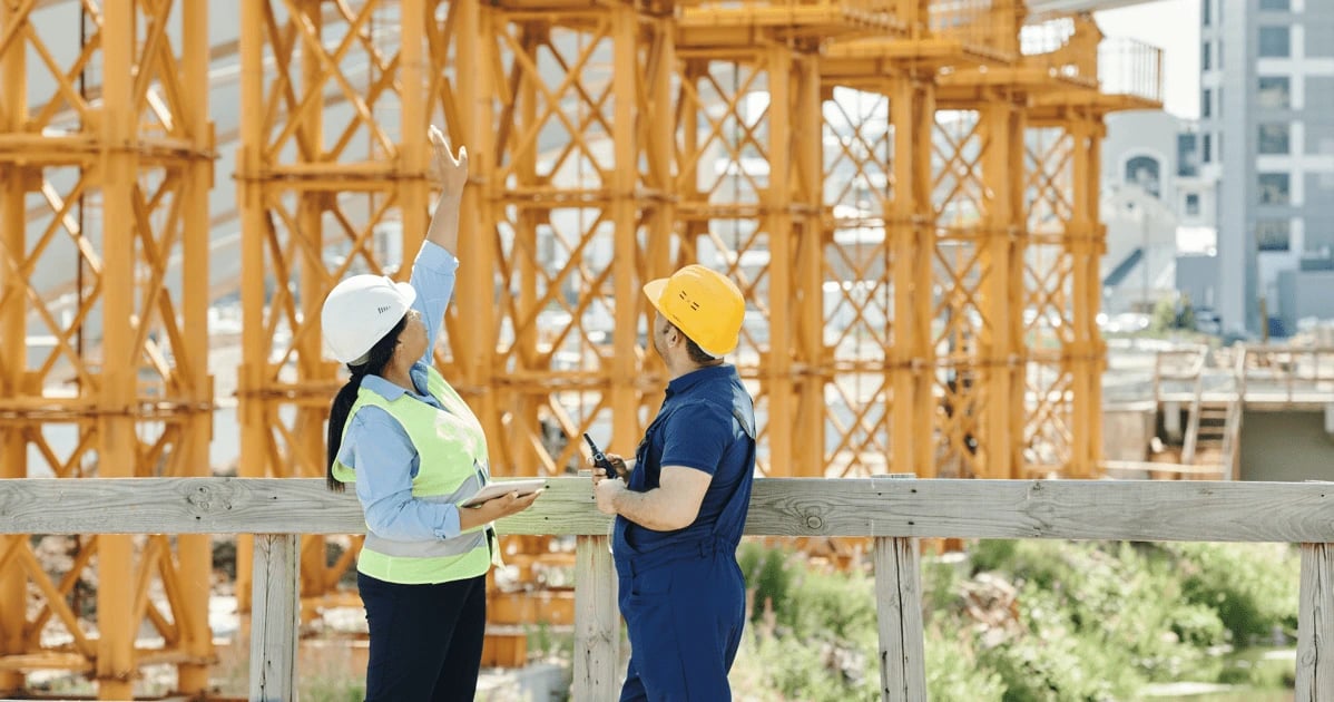 Two individuals wear hard hats discussing a construction project at the building site.