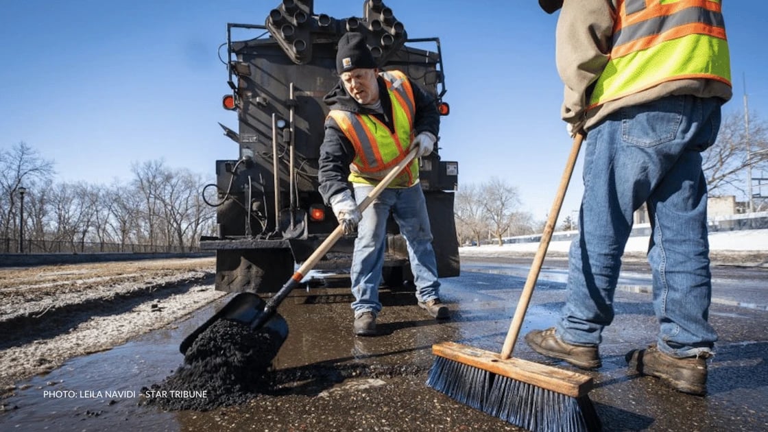 Two workers in safety vests paving a street.